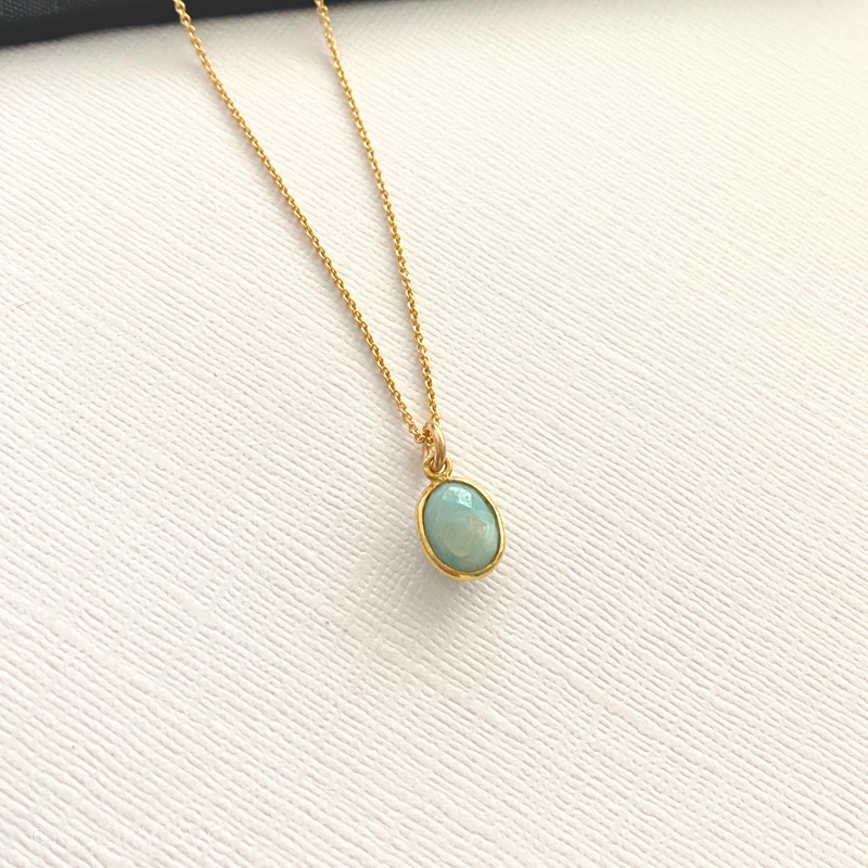Gold necklace with a pale blue pendant on a white background