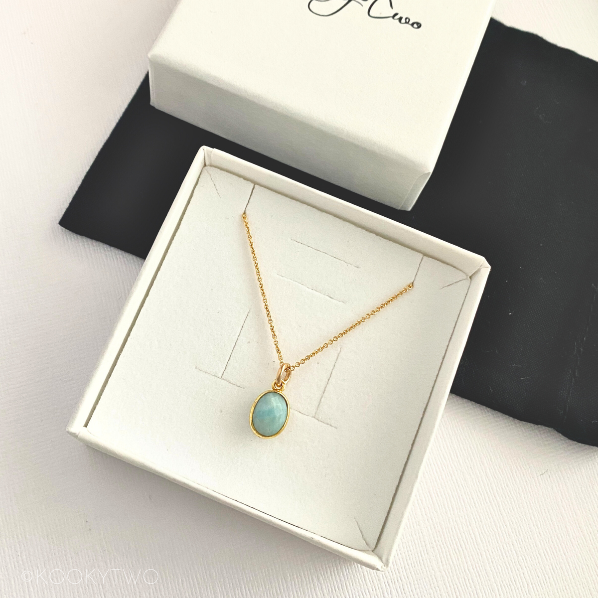 Gold necklace with a Larimar pendant in a white box.