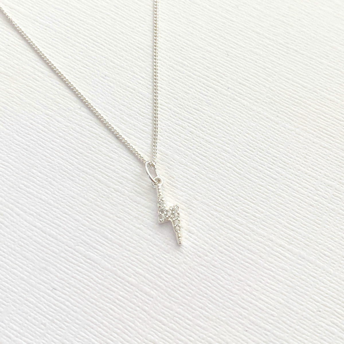 Sterling silver dainty lightning bolt charm necklace on a textured white surface.