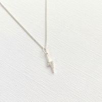 Sterling silver dainty lightning bolt charm necklace on a textured white surface.