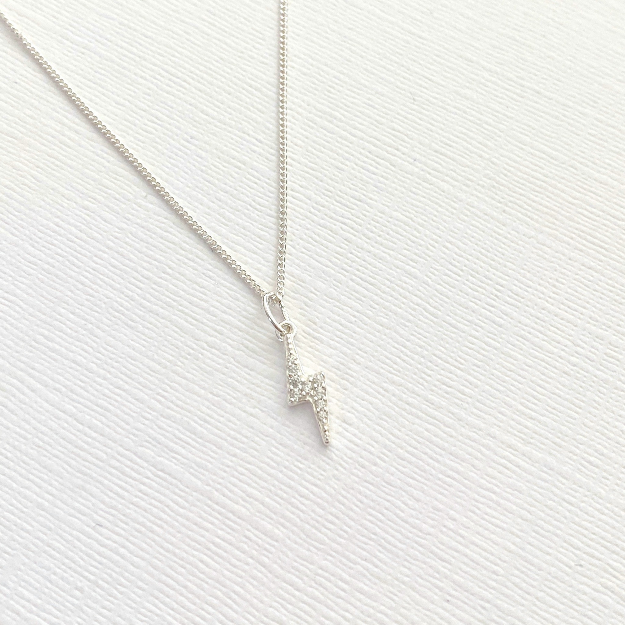 Sterling silver dainty lightning bolt charm necklace on a textured white surface.