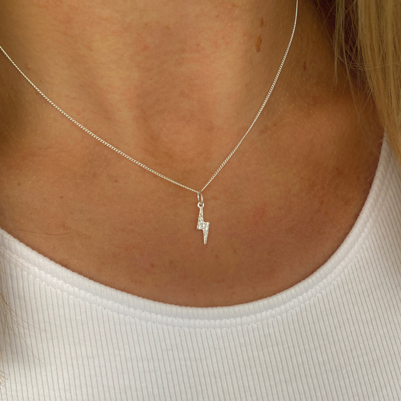 Sterling silver necklace with a small lightning bolt pendant on a person wearing a white top.