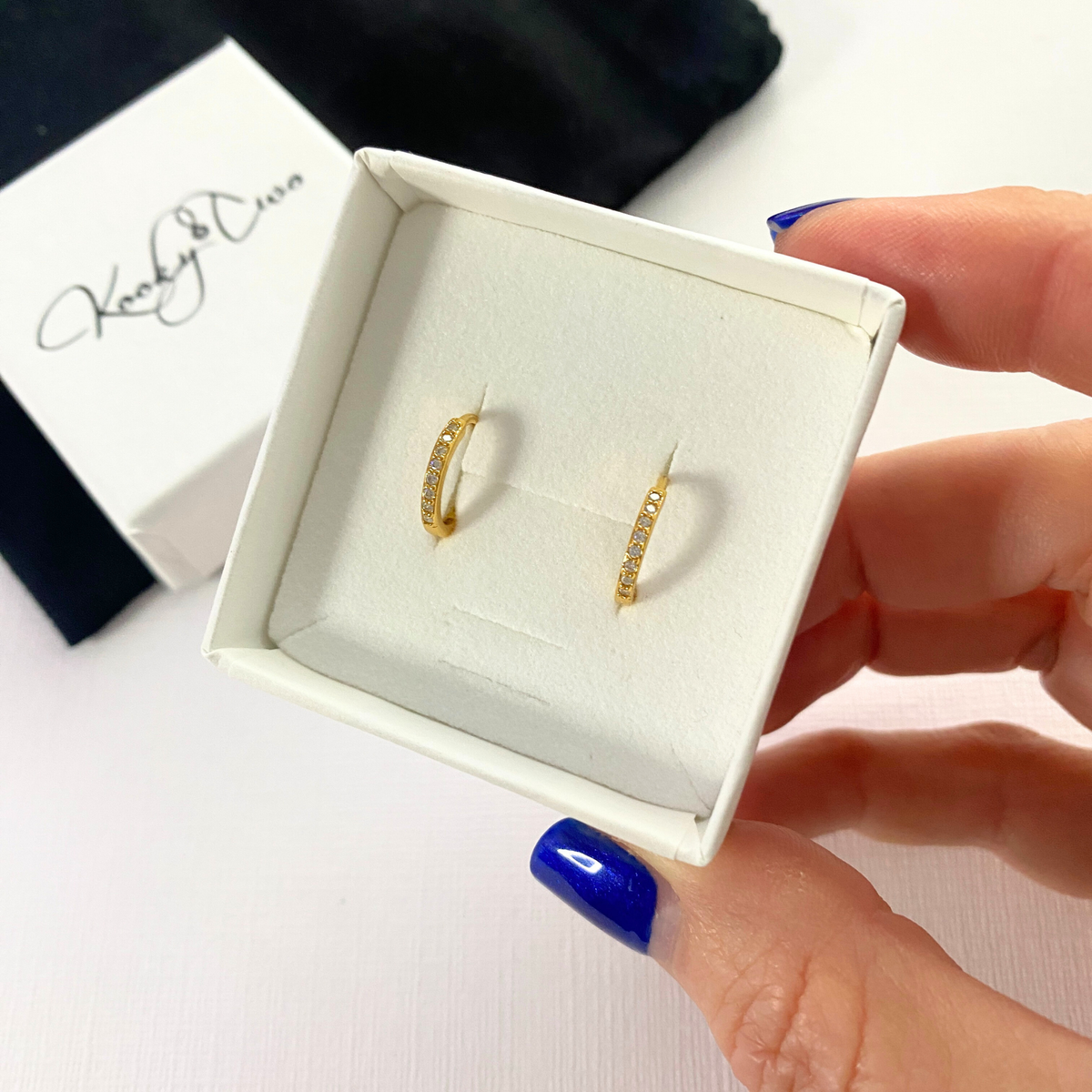 Mini gold hoop earrings with sparkly stones in a white box.