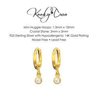 A pair of gold-plated huggie hoop earrings with clear crystal stones, shown below product specifications on a white background. The brand name 'KookyTwo' is visible at the top.