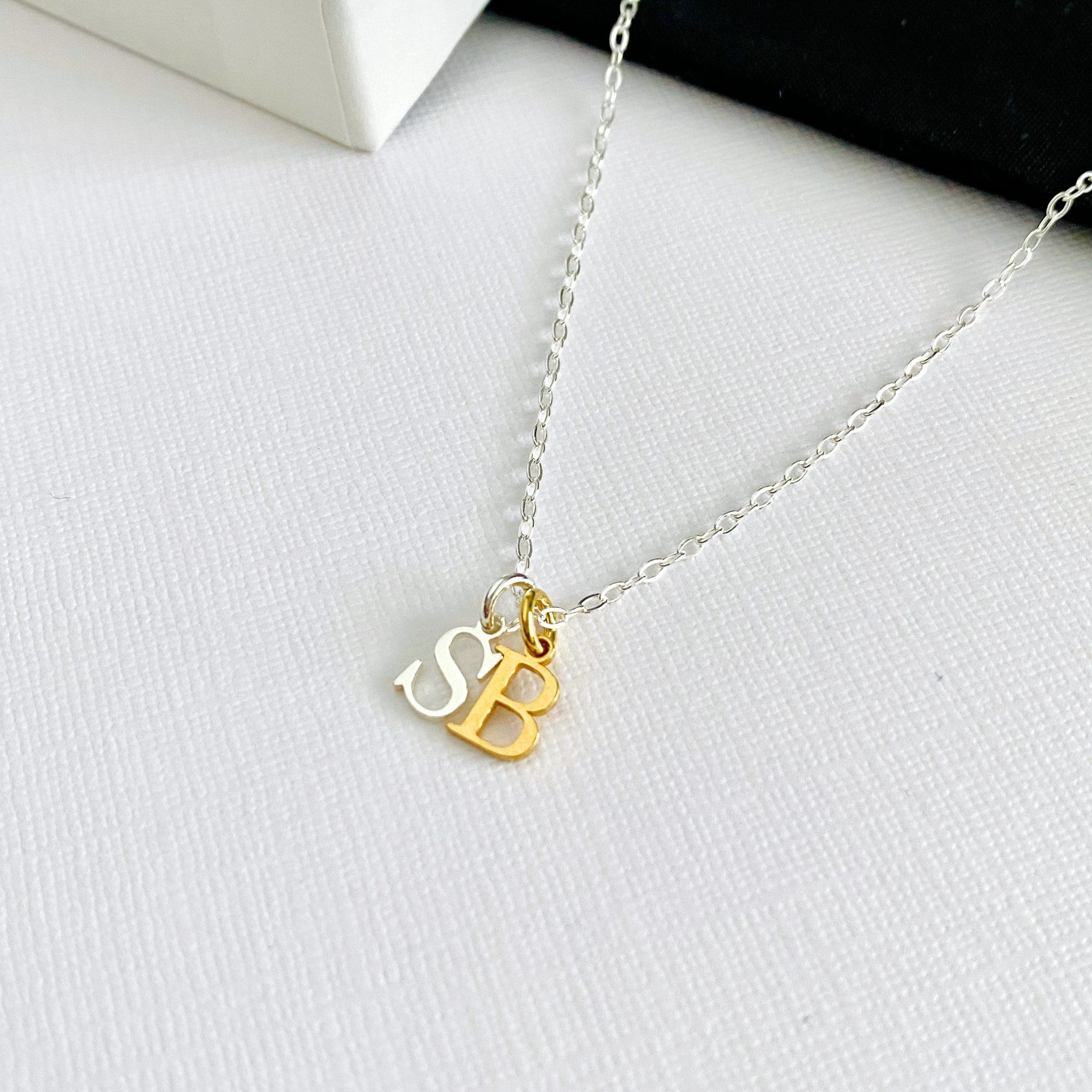 Necklace with gold and silver initial charms in letter S and letter B pendants on a white surface.
