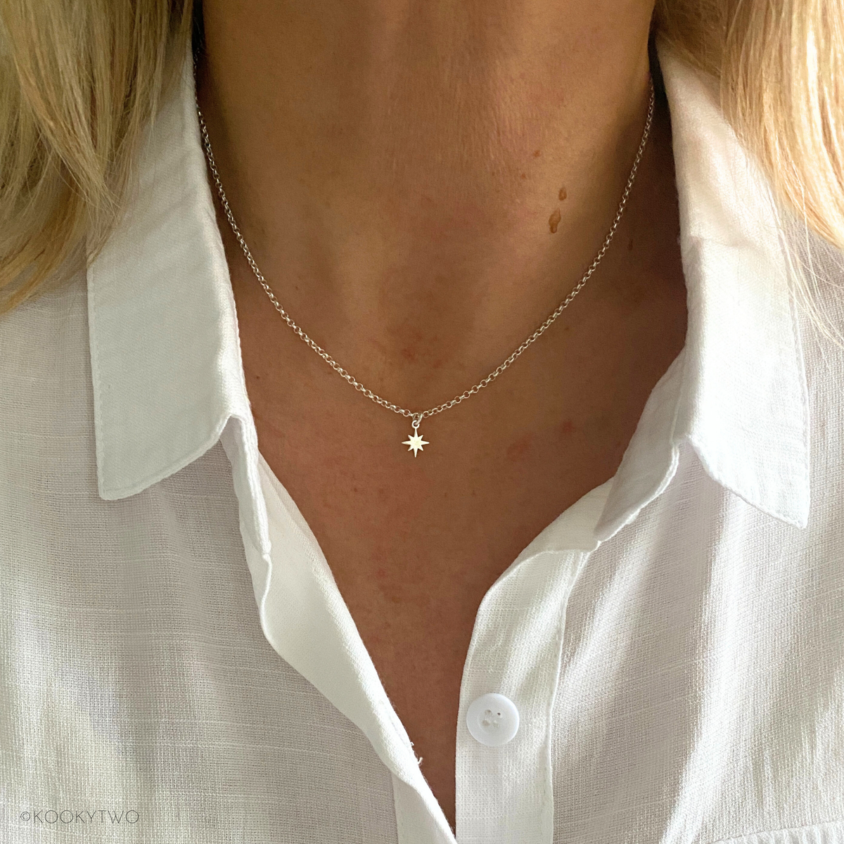 Close-up of a person wearing a silver necklace with a pole star pendant while wearing a white shirt.