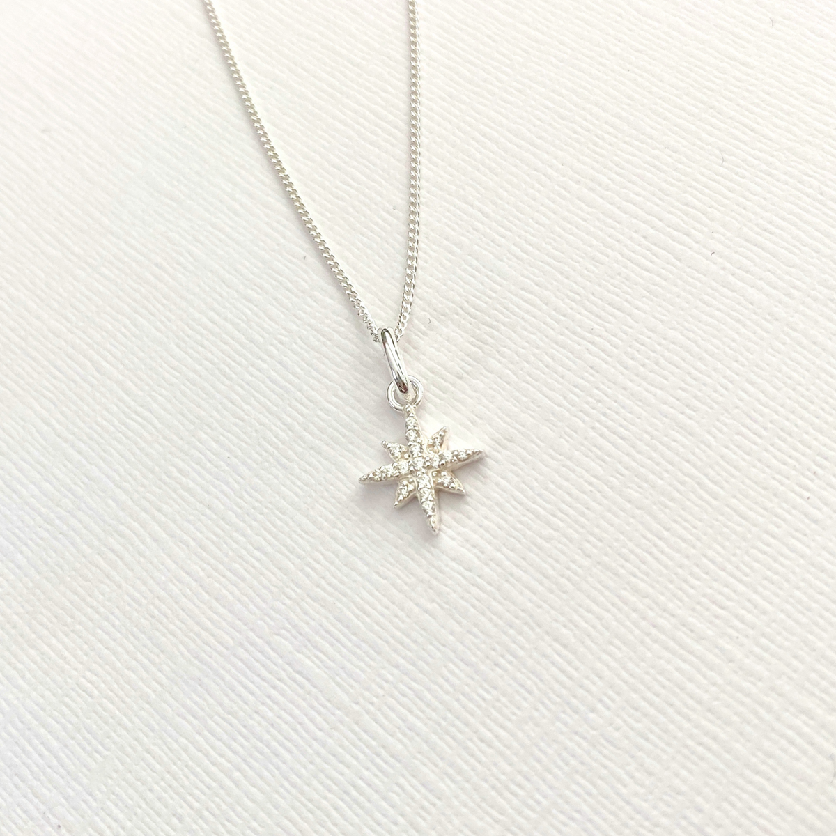 Silver star-shaped pendant with CZ crystals on silver necklace on a white background.