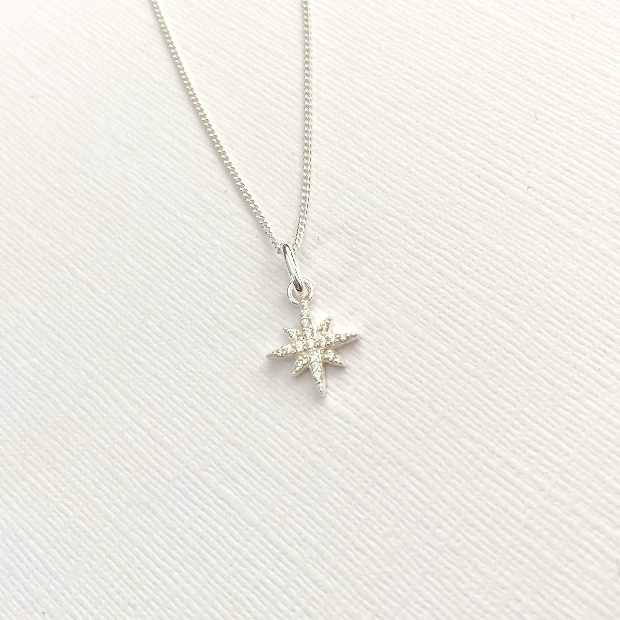 Silver star-shaped pendant with CZ crystals on silver necklace on a white background.