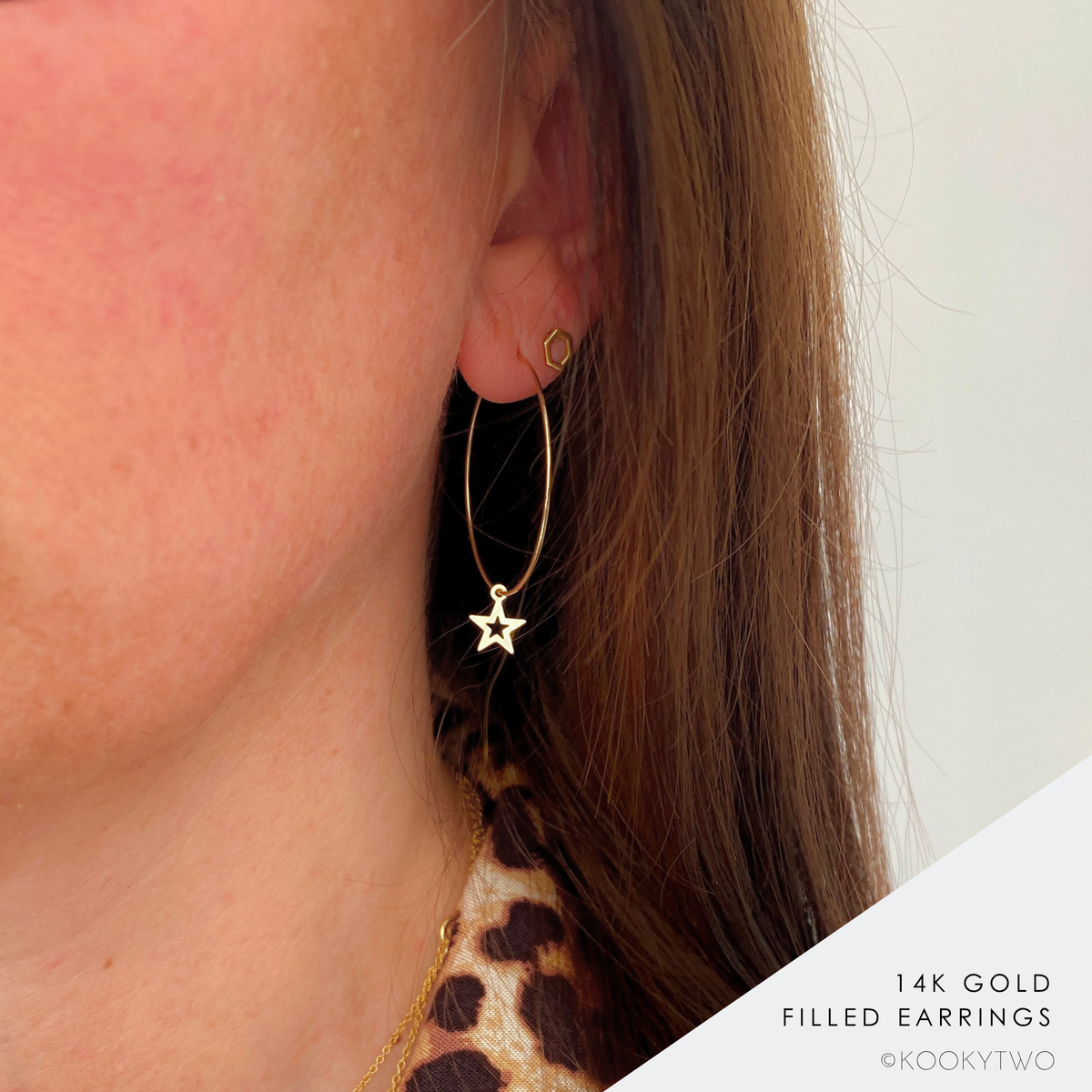 A close-up of a person's ear wearing a large gold hoop earring with a star charm, alongside a small gold stud. The person has light brown hair and a leopard print top, set against a plain light background with a text overlay in the bottom right corner.
