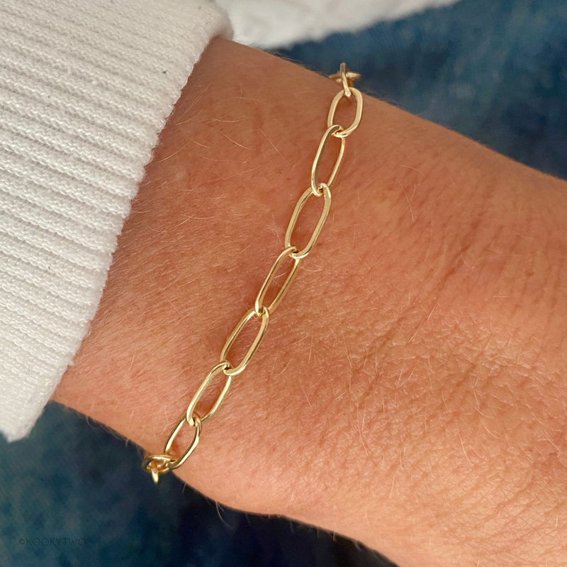 paperclip chain bracelet on a wrist with white top and jeans.