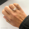 Lady wearing a ring with a pink gemstone, with a plain background. Gemstone is Rose Quartz on sterling silver adjustable ring base.
