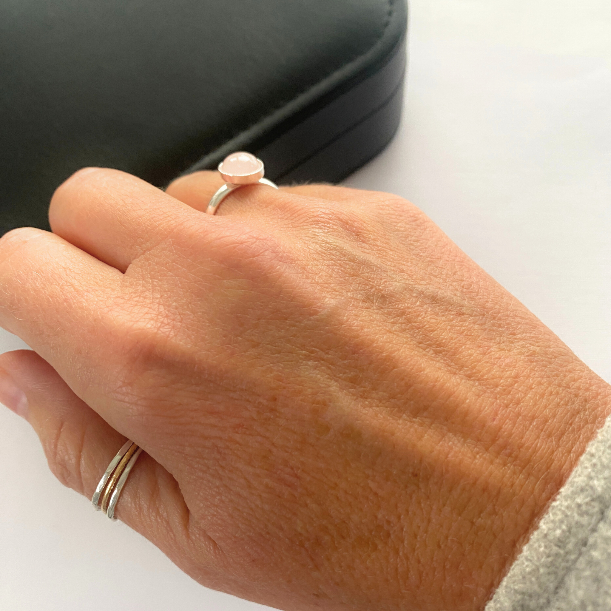 Hand wearing a ring with a pink rose quartz stone on a white background. Rose quartz gemstone sits in an adjustable ring base in sterling silver.