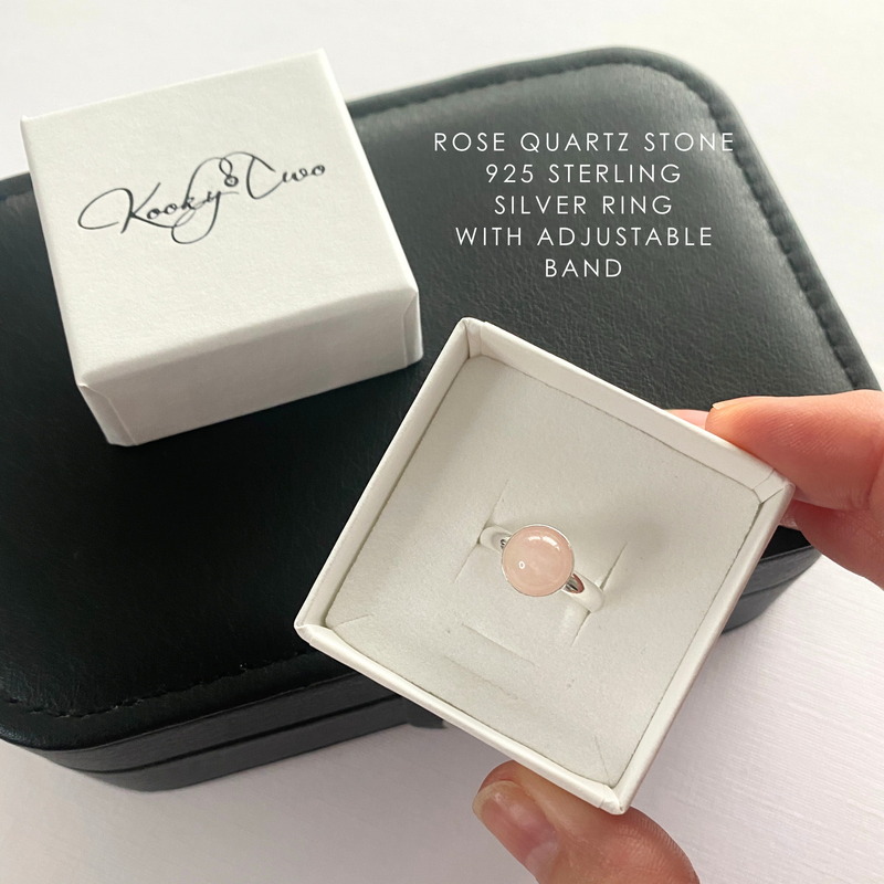 Rose quartz stone ring with adjustable band in a white box, held by a hand.