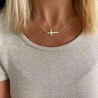 Necklace with a cross pendant worn by a person in a light gray shirt.