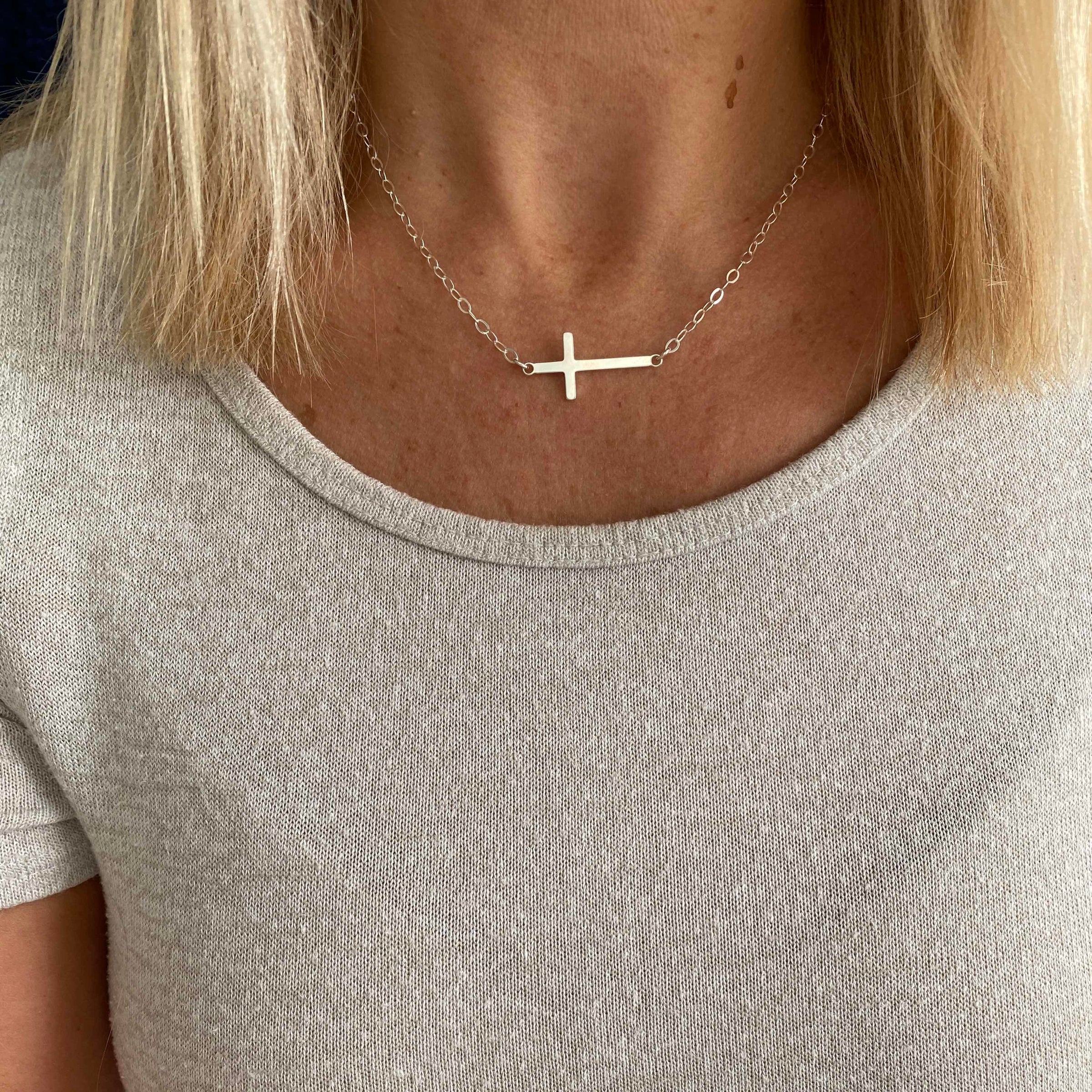 Necklace with a cross pendant worn by a person in a light gray shirt.