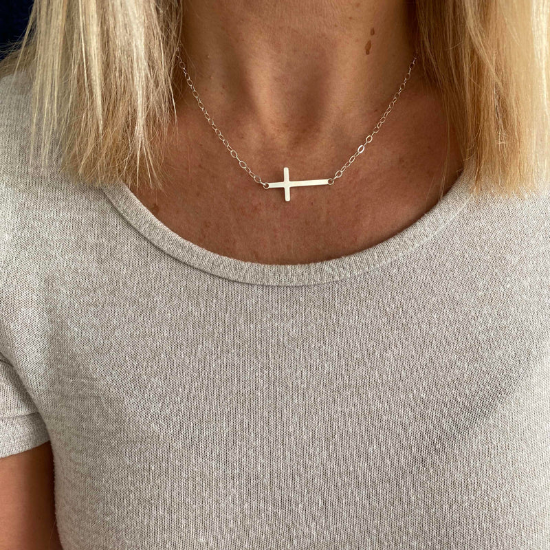 Necklace with a cross pendant worn by a person in a light gray shirt.