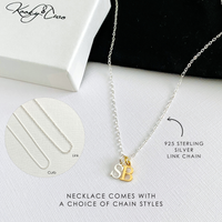Necklace with two monogram initial charms on a white surface with branding and product details.
