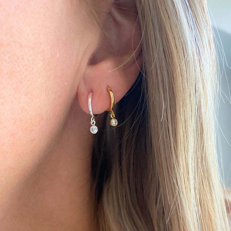 Close-up of a person wearing gold and silver hoop earrings with small crystal charm.