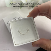 Box with silver and crystal ear jacket with chain between two crystal stones. Branding on box is KookyTwo.