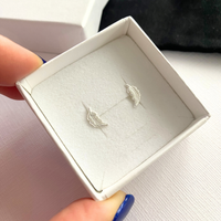 Silver feather earrings in a white box held by a hand with blue nail polish.