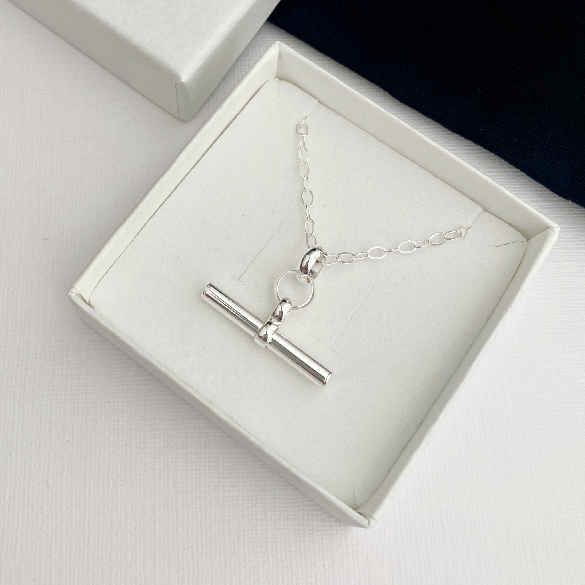 A silver t-bar pendant necklace displayed inside an open white gift box on a white surface.