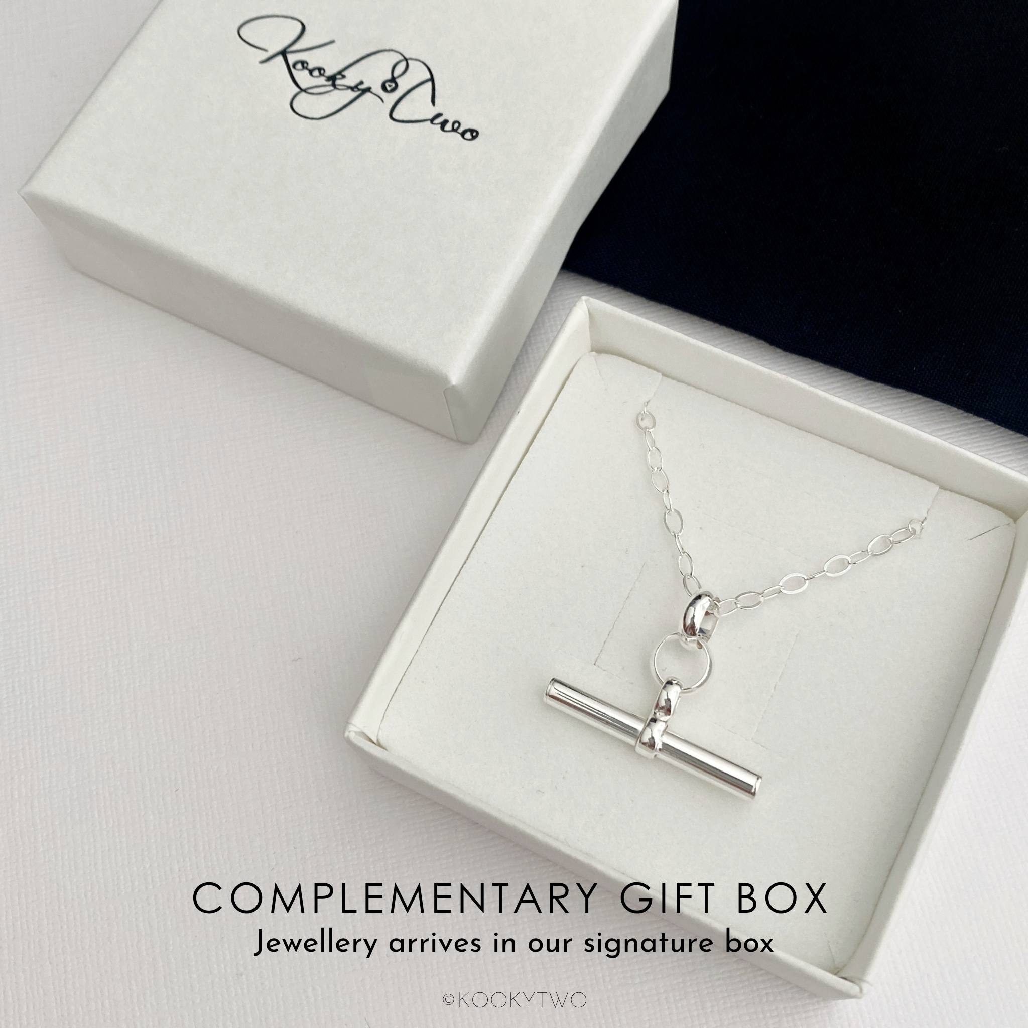A silver pendant necklace displayed in an open white gift box, and the text 'COMPLEMENTARY GIFT BOX' on a light background. The signature 'KooktyTwo' is visible on the closed box.