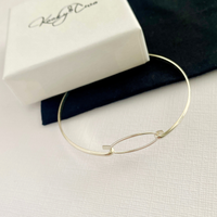 Silver eternity bangle on a white surface with a branded KookyTwo box in the background.