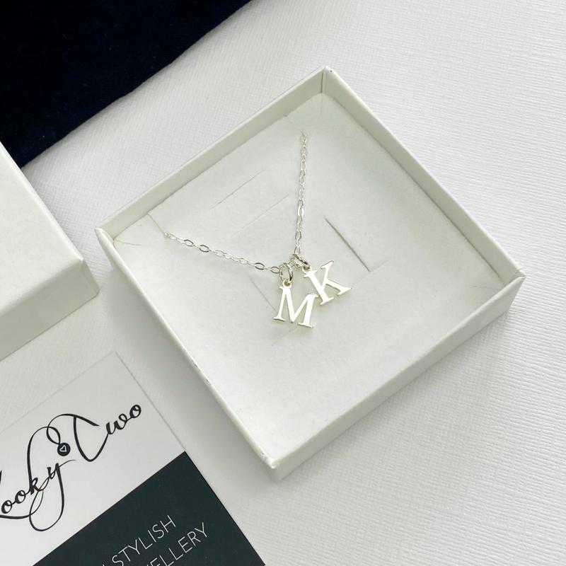 Silver necklace with 'MK' pendant in a white box on a light surface