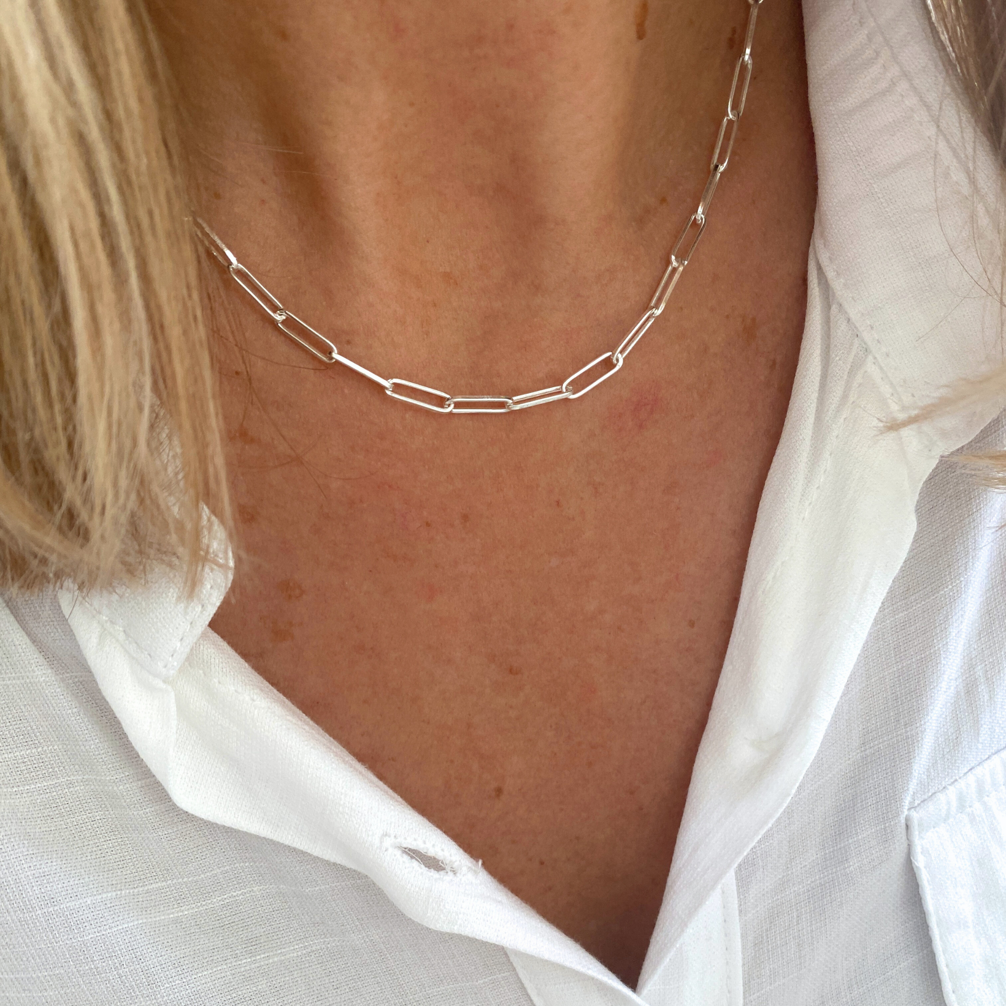 Silver rectangle links chain necklace worn by a person with a white shirt