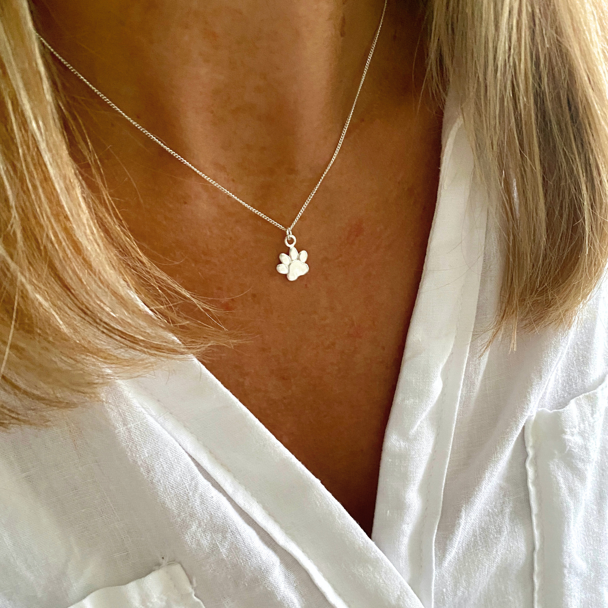Necklace with a paw print pendant worn by a person in a white shirt.
