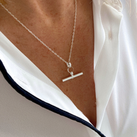 Silver hanging t-bar necklace in sterling silver on a person wearing a white shirt.