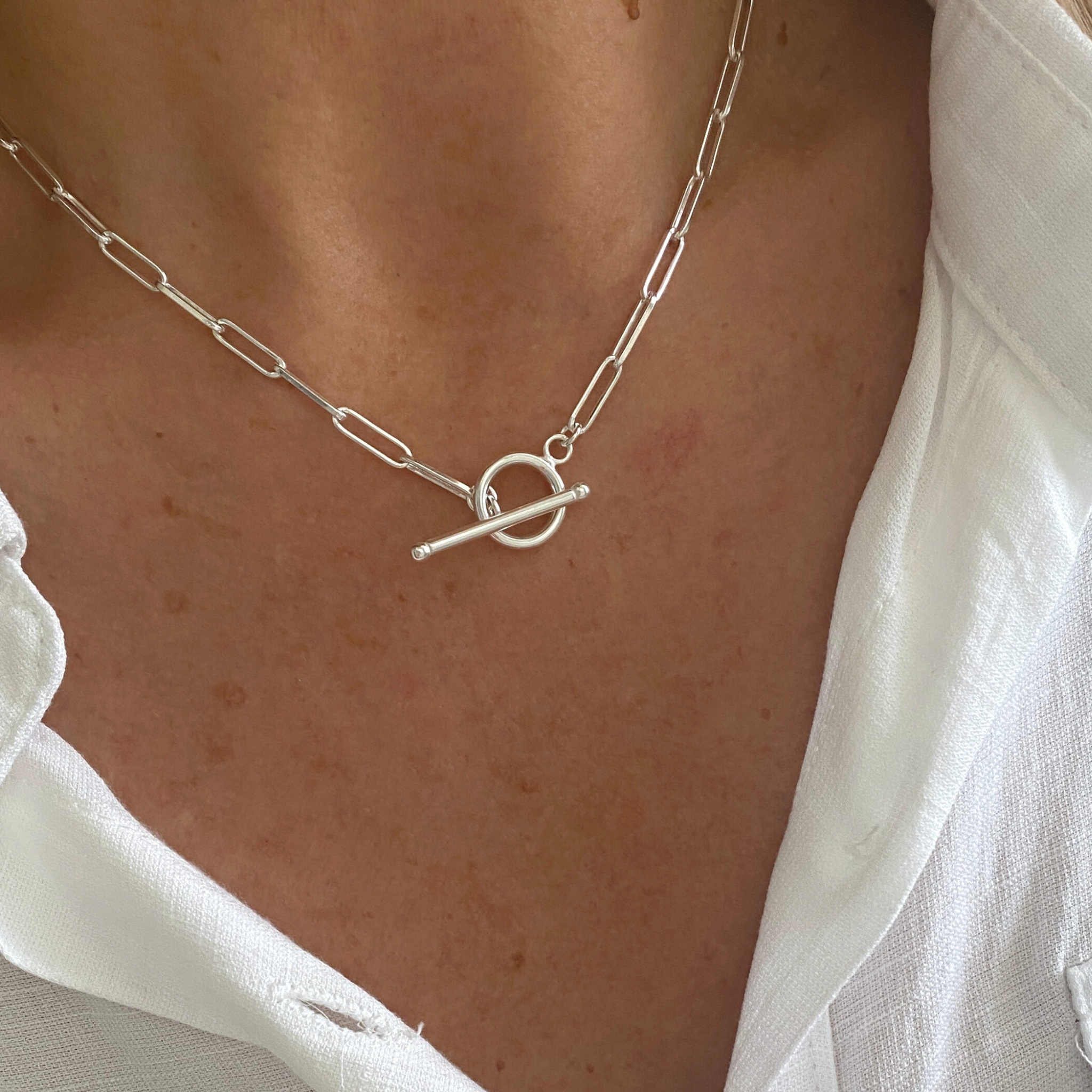 Silver necklace with a toggle bar pendant worn by a person in a white shirt.