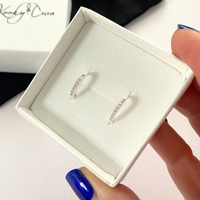Silver earrings with crystals in a white box held by a hand.