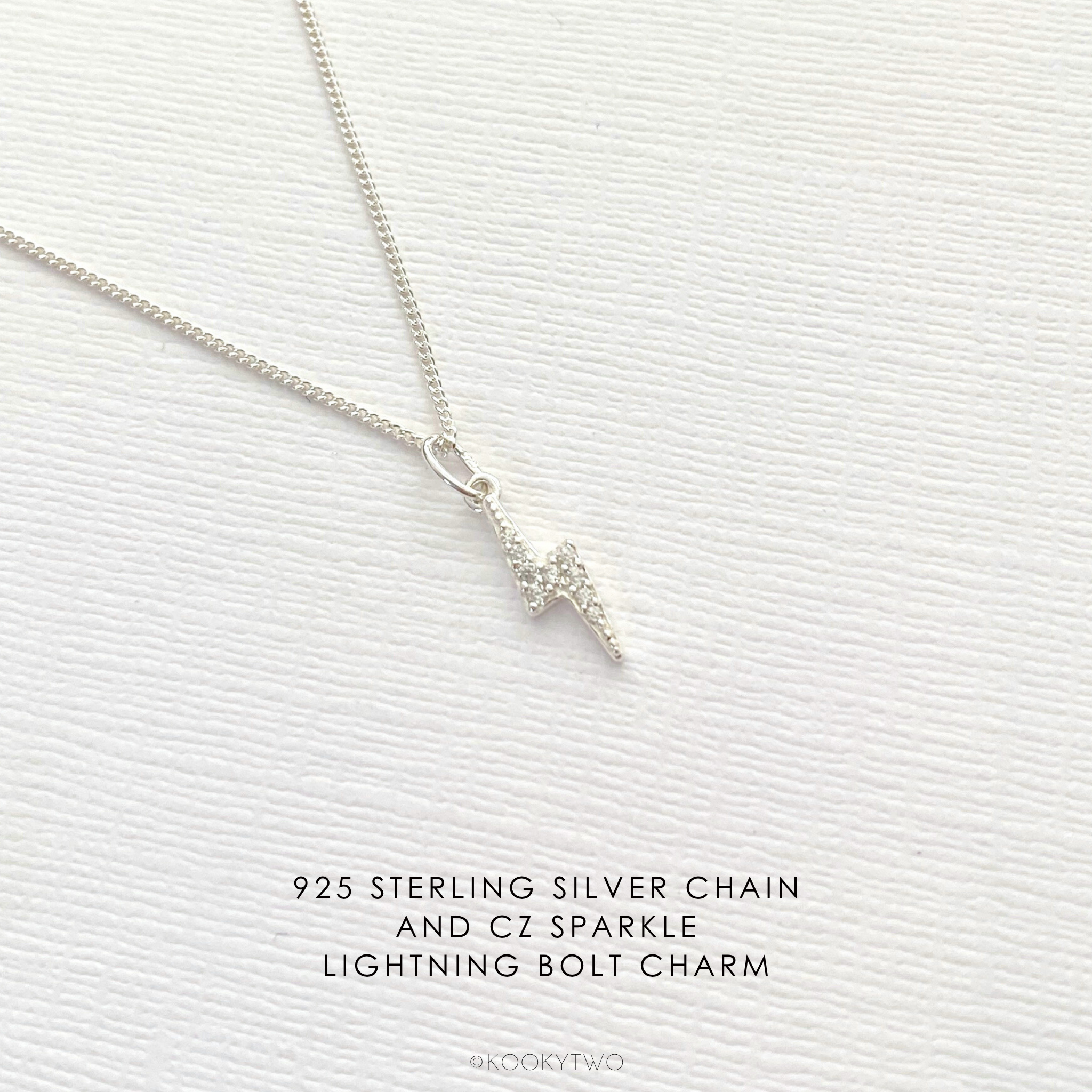 Sterling silver necklace with sparkle lightning bolt charm on a textured white background.