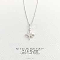 Silver sparkle star necklace with a north star charm on a white fabric background.