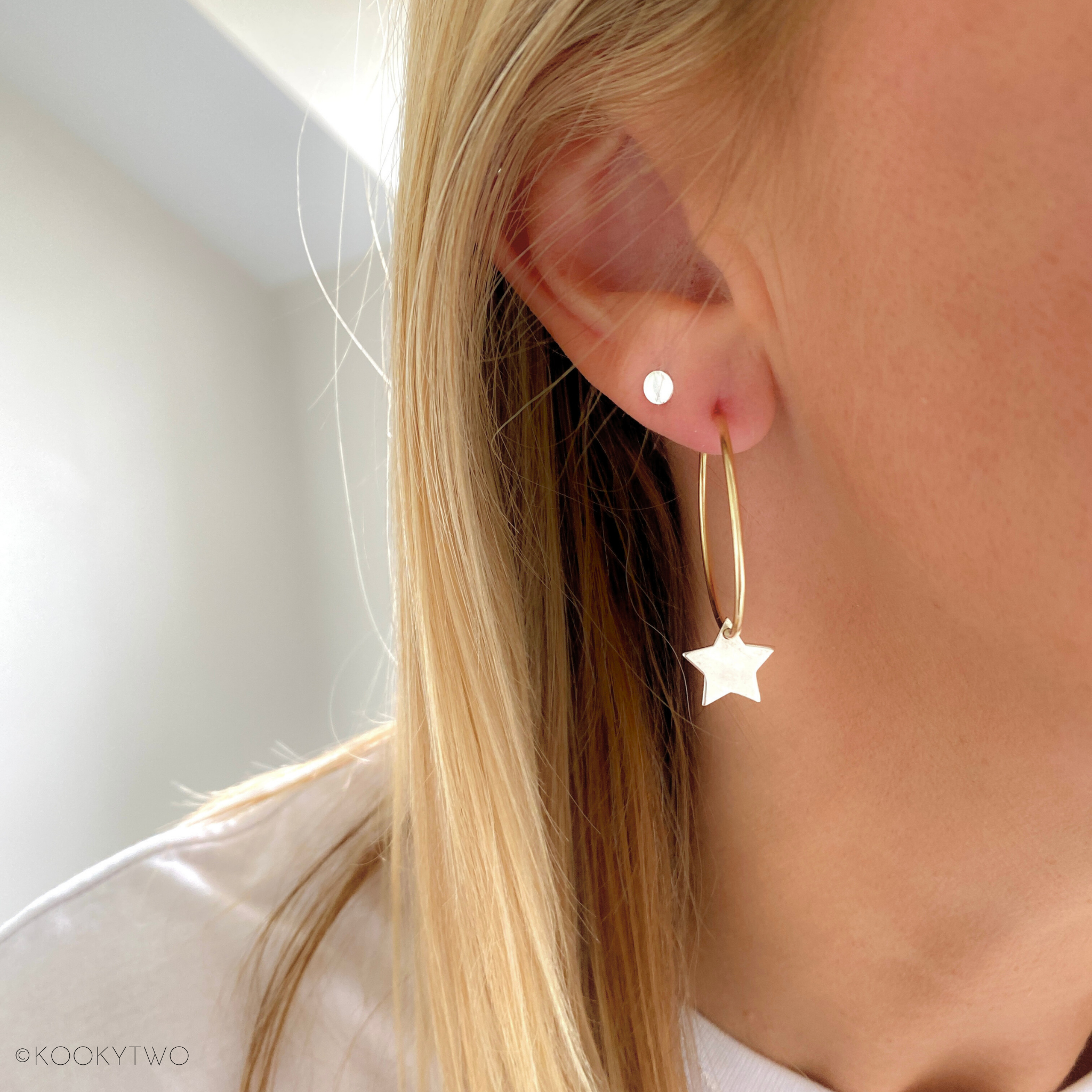 Ladies gold hoop earrings with star charm hanging down, stacked with plain silver earring stud.