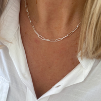 Silver paperclip chain necklace worn by a person with a white shirt
