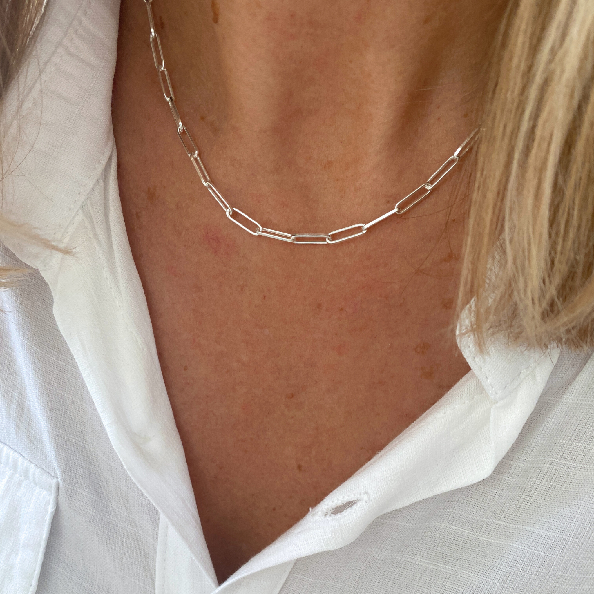 Silver paperclip chain necklace worn by a person with a white shirt