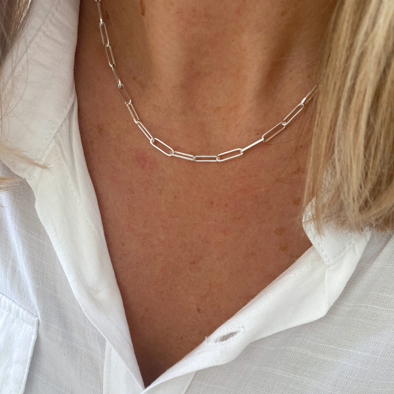 Silver paperclip chain necklace worn by a person with a white shirt