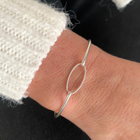 Silver slim bangle bracelet on a wrist with a white textured cardigan.