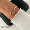Silver slim bracelet on a wrist with a white long-sleeve top.