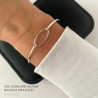 Silver slim bracelet on a wrist with a white long-sleeve top.