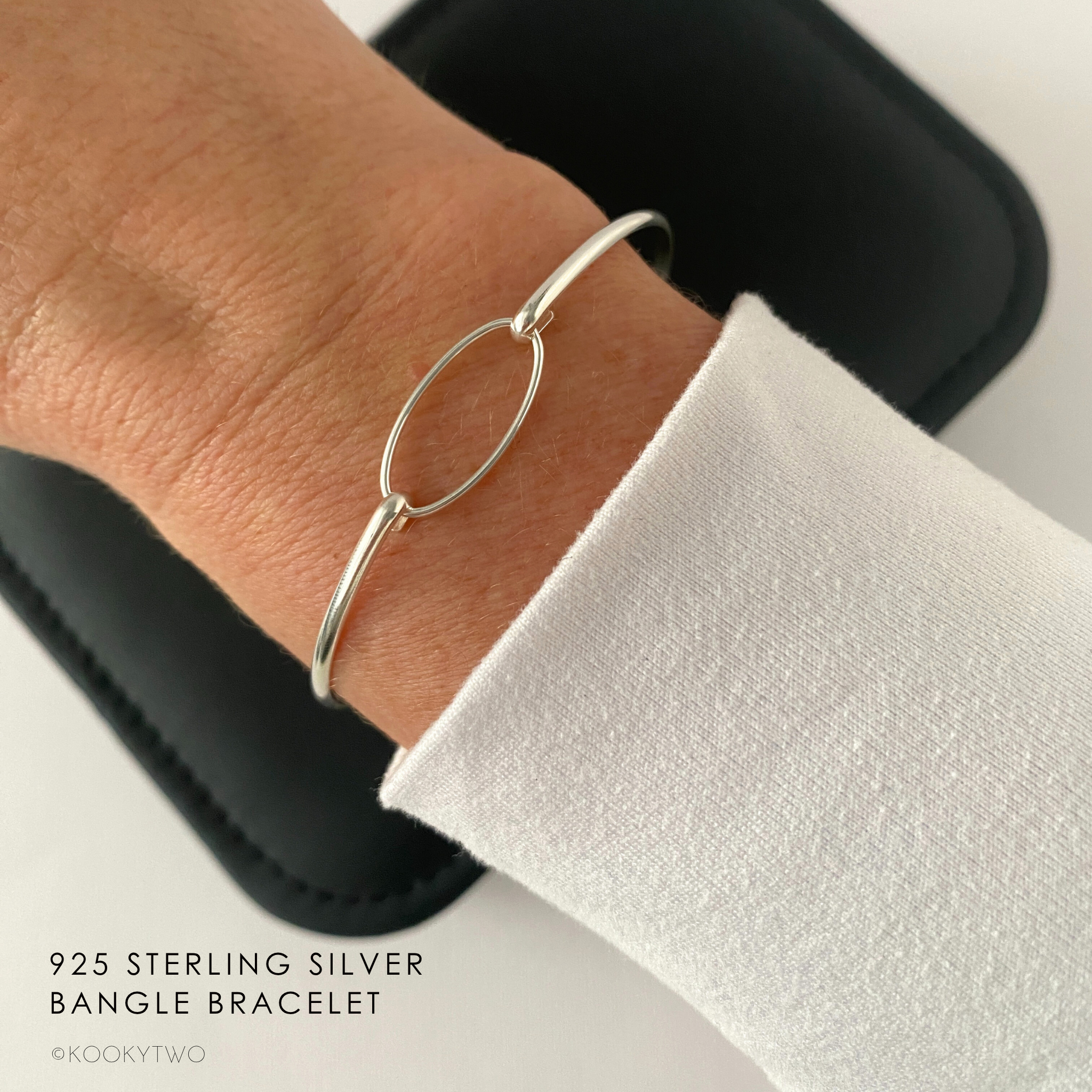Silver slim bracelet on a wrist with a white long-sleeve top.