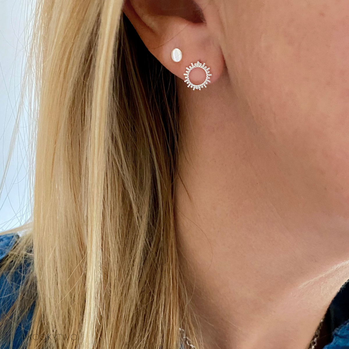Close-up of sun-shaped sterling silver stud earrings on person. KookyTwo.