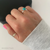 Hand wearing ring with turquoise stone and sterling silver band on a white background.