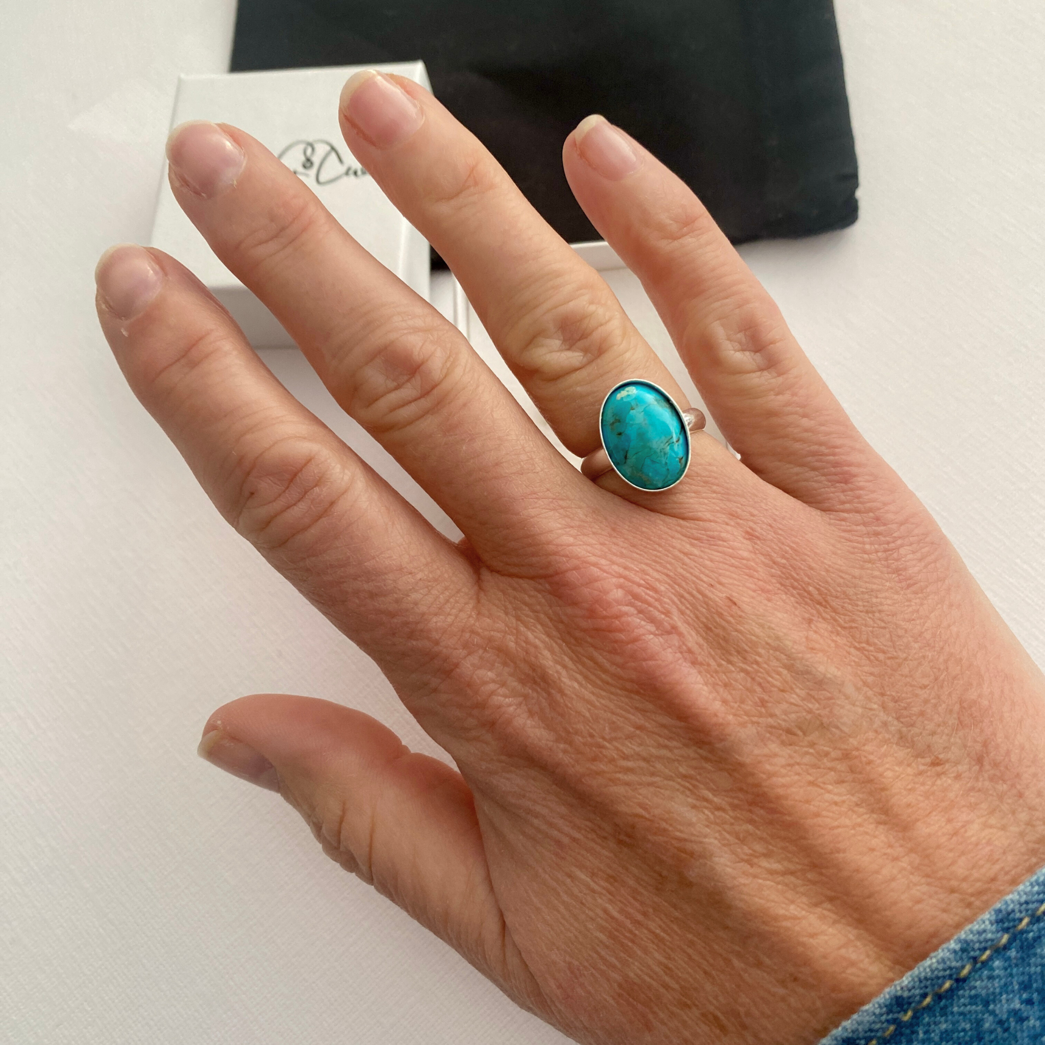 Hand wearing a oval turquoise ring on a white background