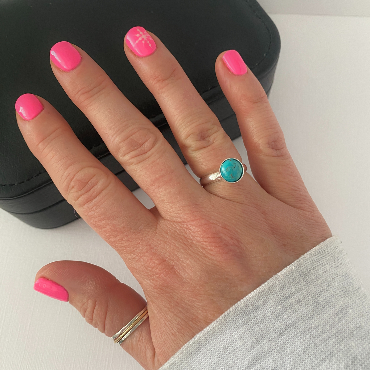 Hand wearing an adjustable turquoise silver ring with a turquoise gemstone on a white background.
