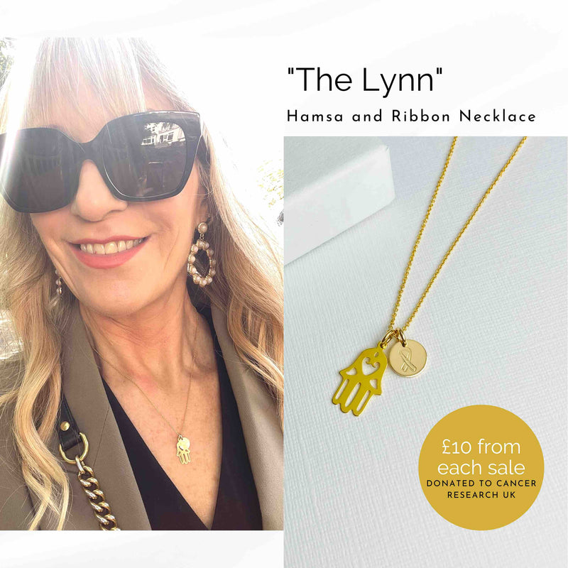 Gold necklace featuring gold hams hand and ribbon disc to represent support of those with cancer.