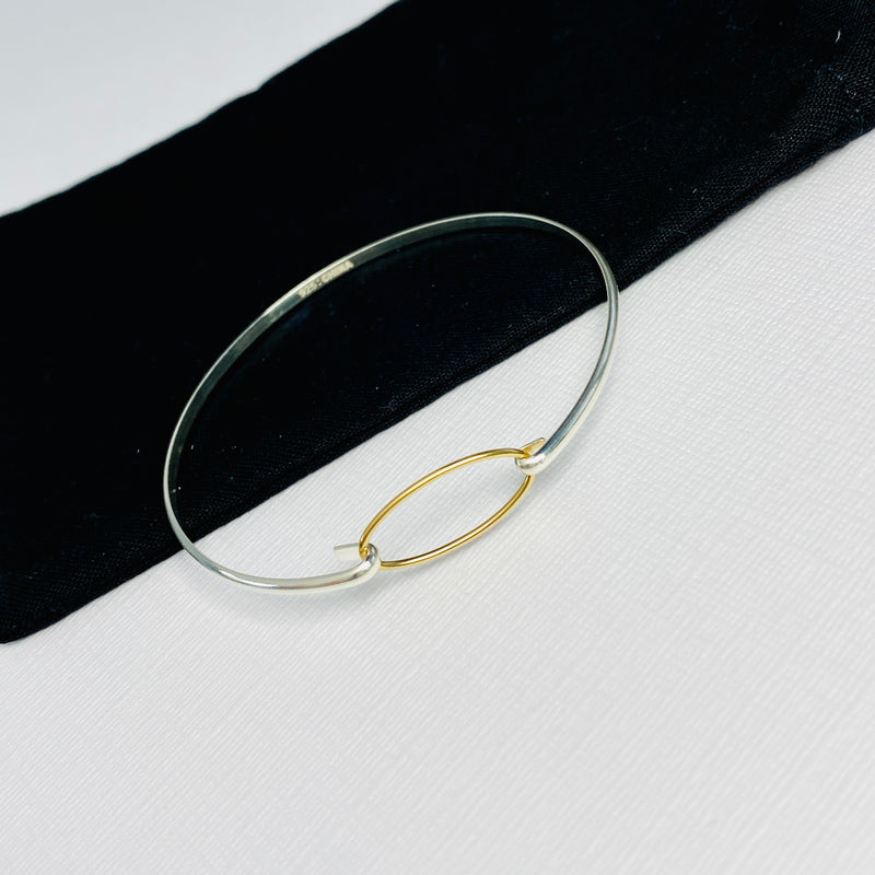 Sterling silver bangle with gold link charm.