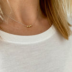 Dainty silver necklace with three shiny gold beads that move freely along the chain. Kooky Two.